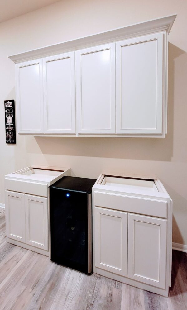 A kitchenette with white cabinets, a wine cooler, and a trash bin compartment features exceptional custom furnishing.