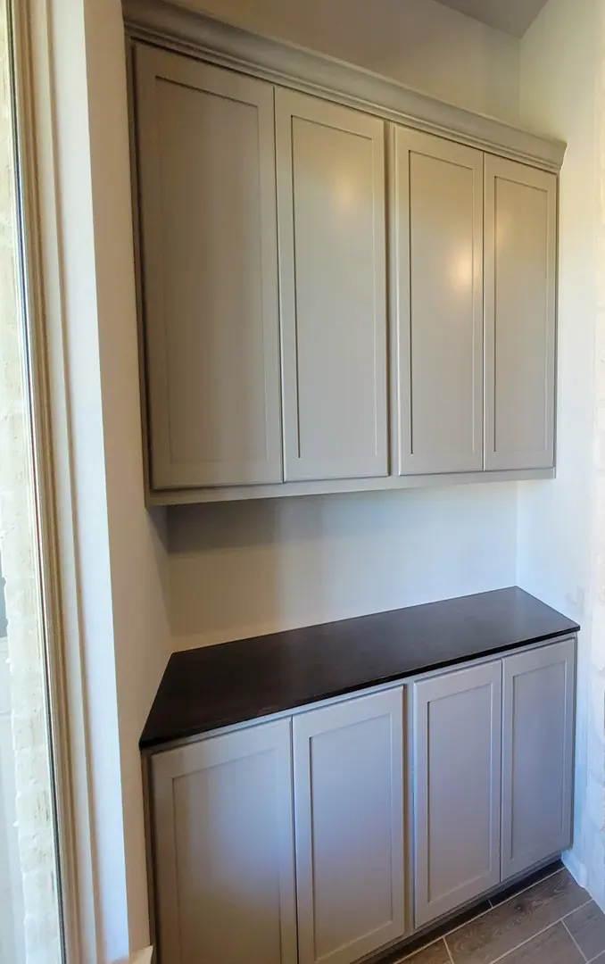 A set of upper and lower beige cabinets with a dark countertop against a light-colored wall, showcasing exceptional custom furnishing.