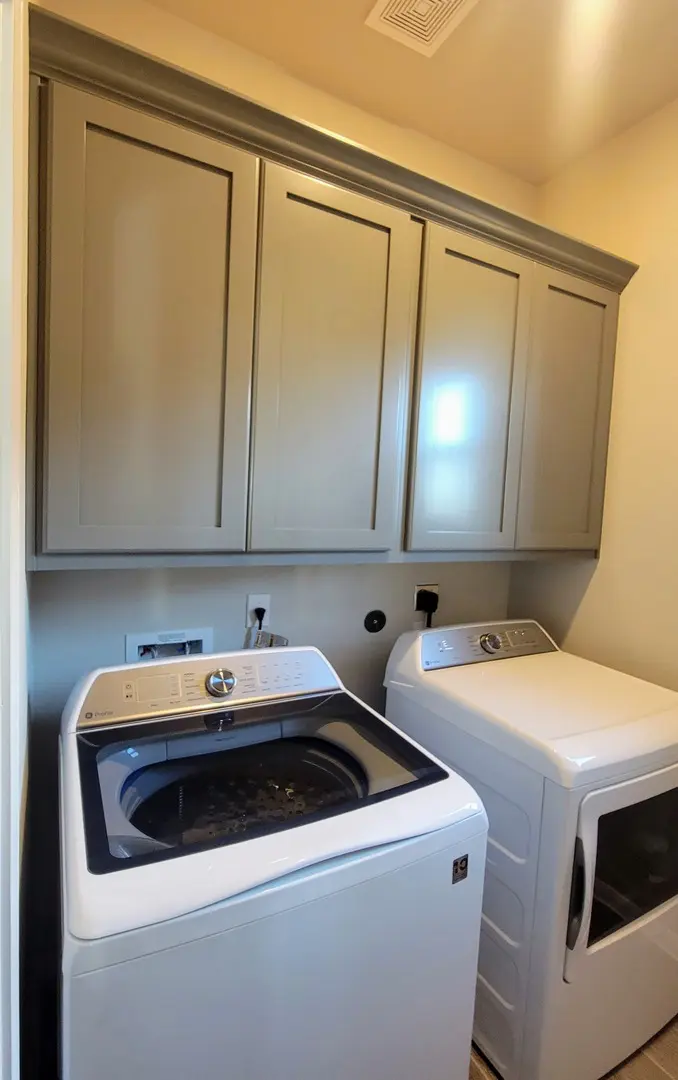 Laundry room with a top-loading washing machine and a front-loading dryer, featuring exceptional custom furnishing overhead cabinets.