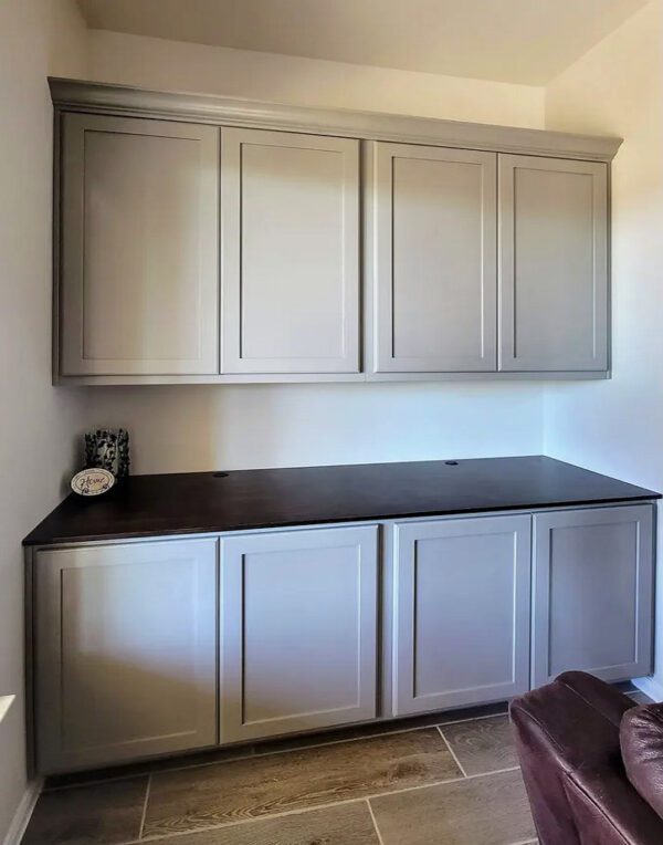 A modern kitchenette with gray cabinets and a dark countertop, featuring exceptional custom furnishing.