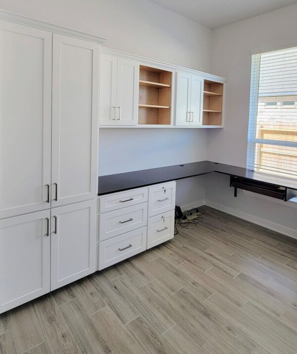 A modern home office with white cabinetry, built-in shelves, and an exceptional custom furnishing black desk area.