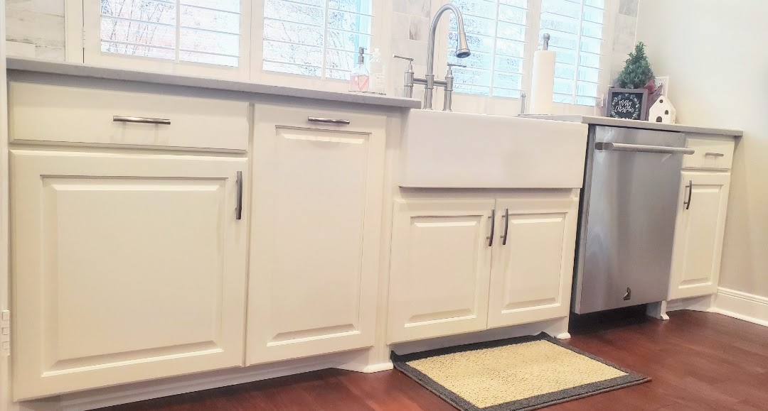 White kitchen cabinetry with modern handles, featuring a farmhouse sink, exceptional custom furnishing, and a stainless steel dishwasher.