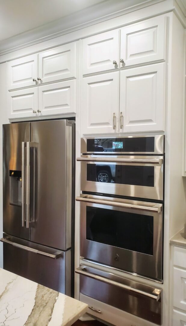 Stainless steel refrigerator and built-in double ovens integrated into white kitchen cabinetry, featuring exceptional custom furnishing.