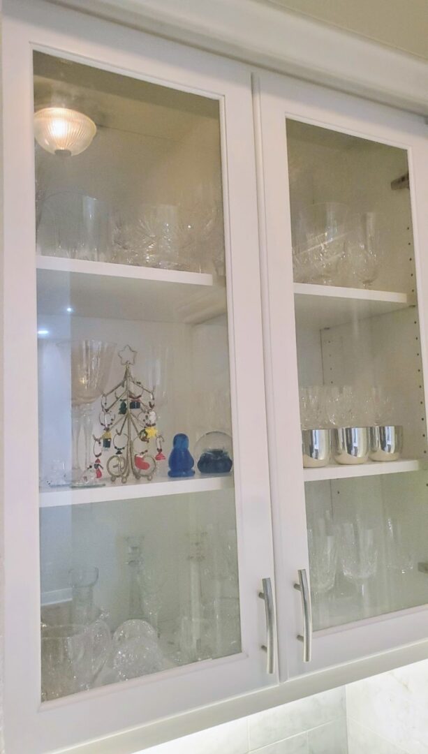 A cabinet with glass doors displaying various glassware and a small decorative item, showcasing exceptional custom furnishing.