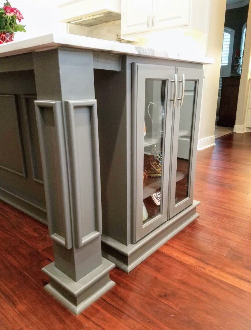 Kitchen island with glass-fronted cabinet and decorative panels in a home with hardwood flooring, featuring exceptional custom furnishing.