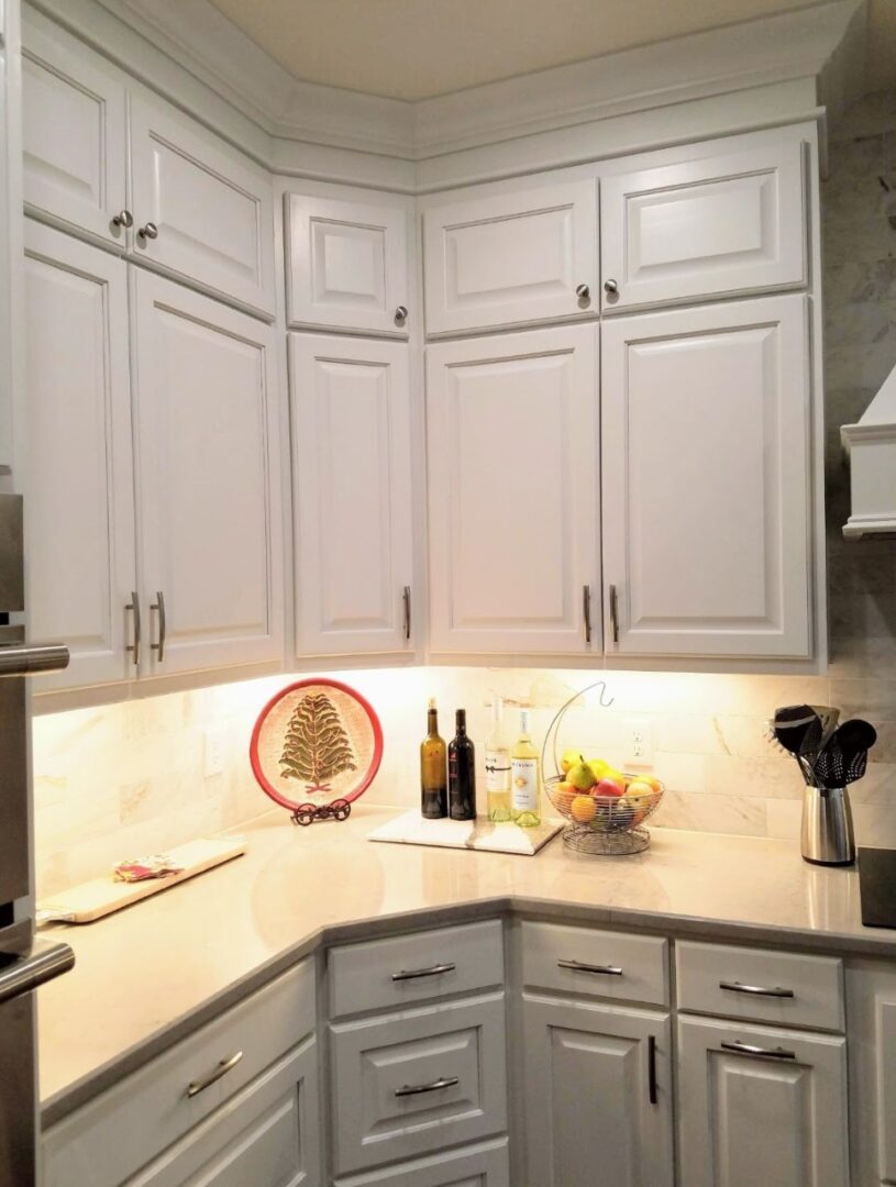 Corner of a modern kitchen with exceptional custom furnishing, including white cabinetry, stainless steel appliances, and a bowl of fruit on the countertop, with a red circle highlighting an area of the backs