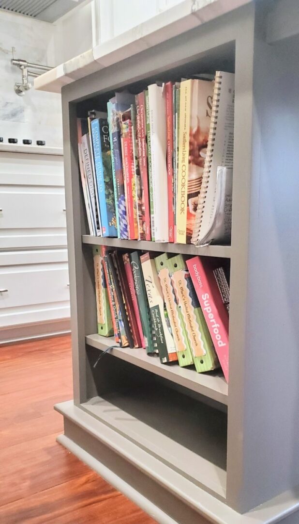 A small bookshelf filled with various cookbooks in a kitchen setting features exceptional custom furnishing.