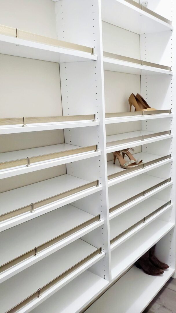 Almost empty white shelves in a store with only a few pairs of exceptional custom furnishing shoes displayed.