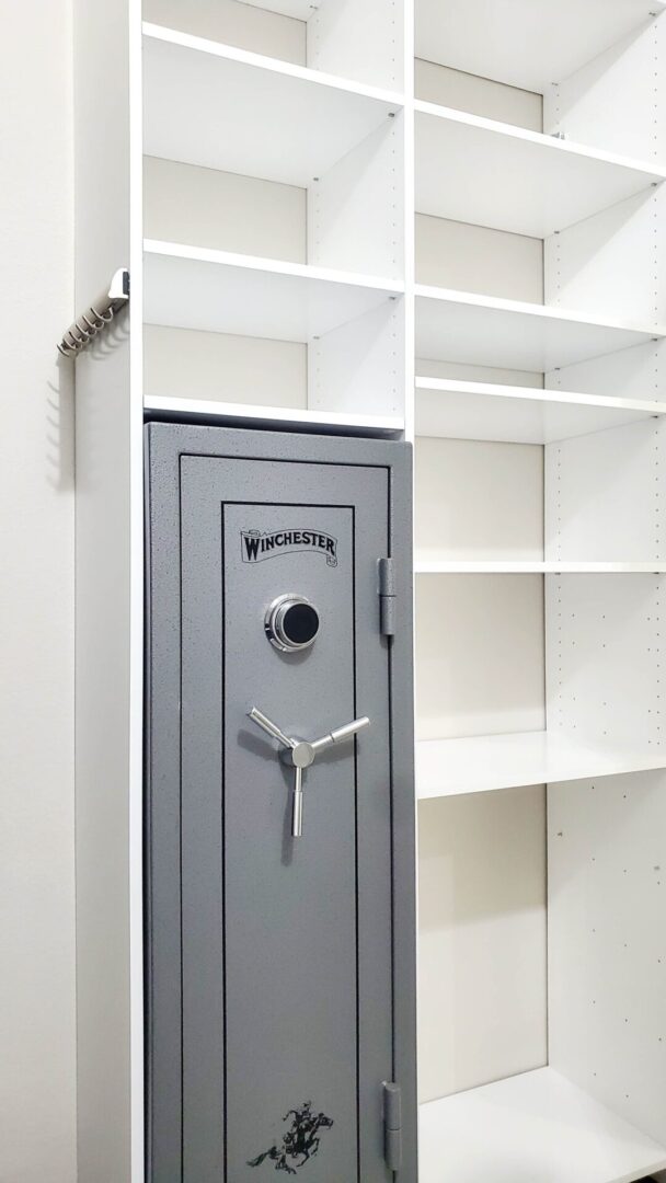 A tall winchester safe standing between white empty shelves, an example of exceptional custom furnishing.