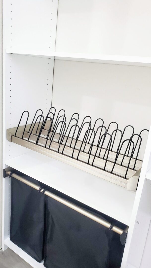 Empty wire rack on a white shelf in an exceptional custom furnishing storage unit with hanging black fabric bins below.