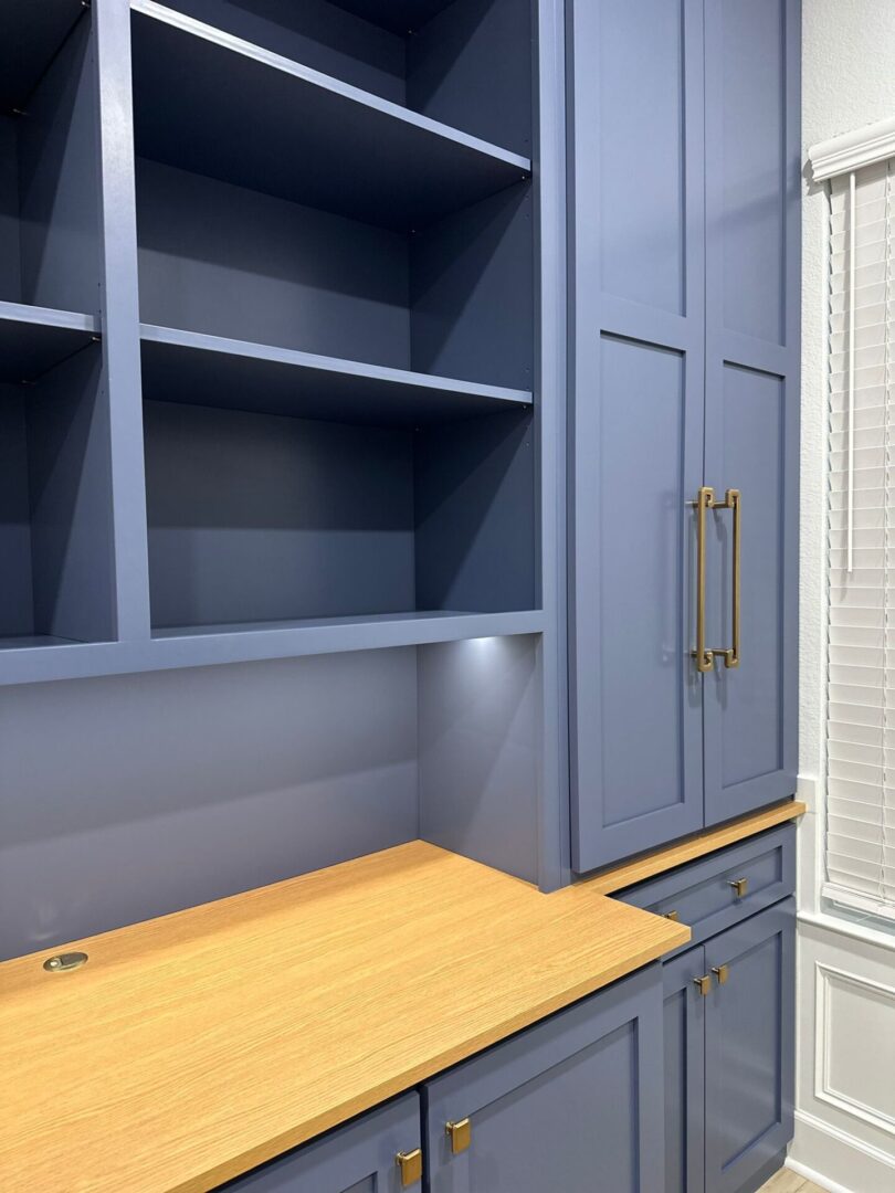 An empty blue built-in shelving unit above a wooden desk with exceptional custom furnishing cabinets.
