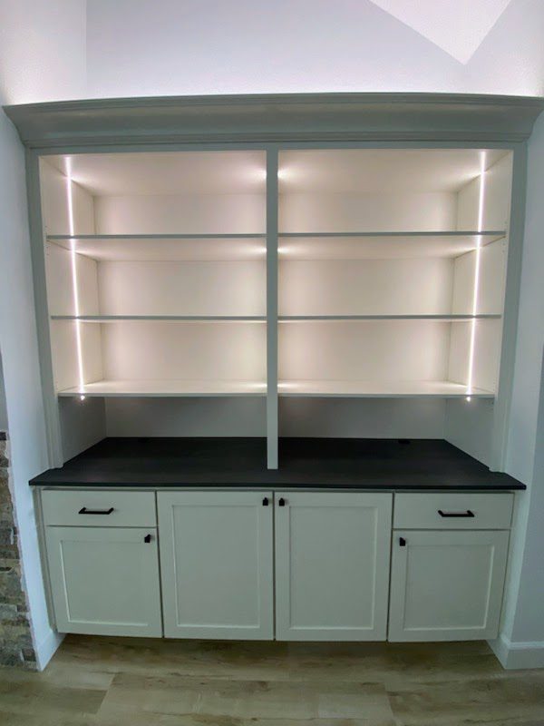 Built-in white bookshelf with cabinet base and exceptional custom furnishing led shelf lighting in a modern interior.