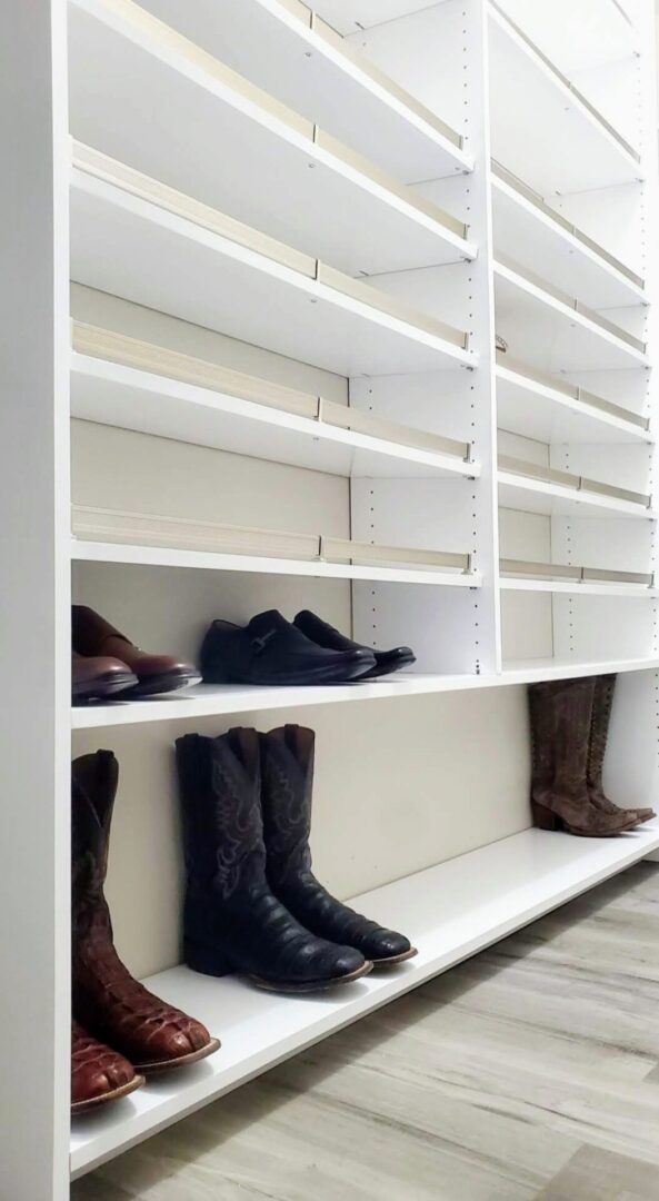 Empty white shelves, part of an exceptional custom furnishing collection, with a few pairs of shoes, including boots and dress shoes.