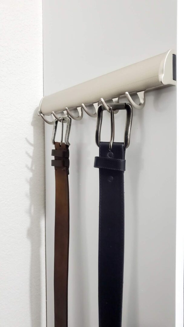 Belts hanging on hooks against a white wall showcase exceptional custom furnishing.