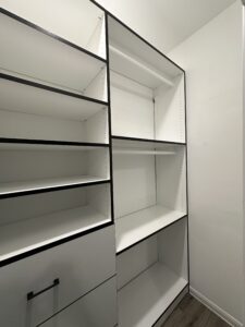 An empty, white modern bookshelf with black framing in a bright room, showcasing exceptional custom furnishing.