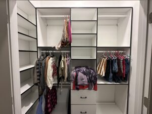 A modern walk-in closet with neatly organized clothes and storage drawers features exceptional custom furnishing.