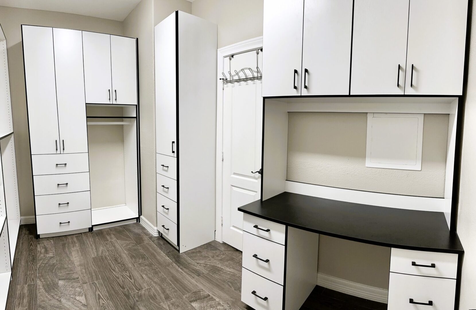 A modern home office with white cabinetry and a black desktop, featuring ample storage and a built-in desk area.