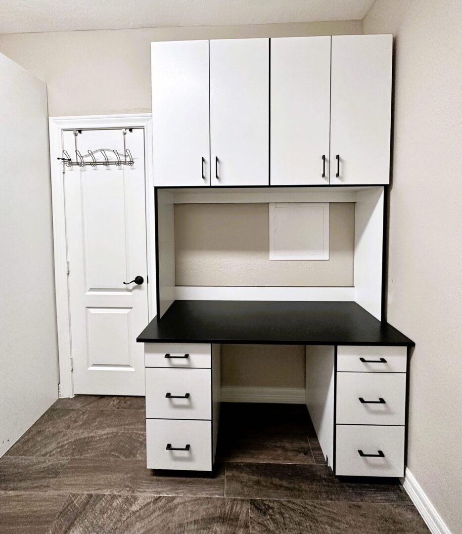 A white and black home office desk with drawers and overhead cabinets, in a room with laminate flooring.