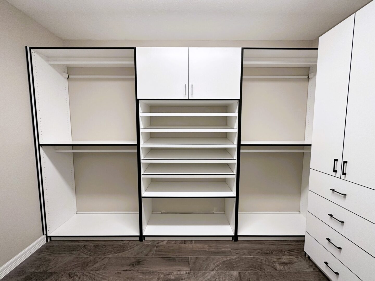 Modern, empty white built-in closet system with shelves and drawers in a room with gray flooring.