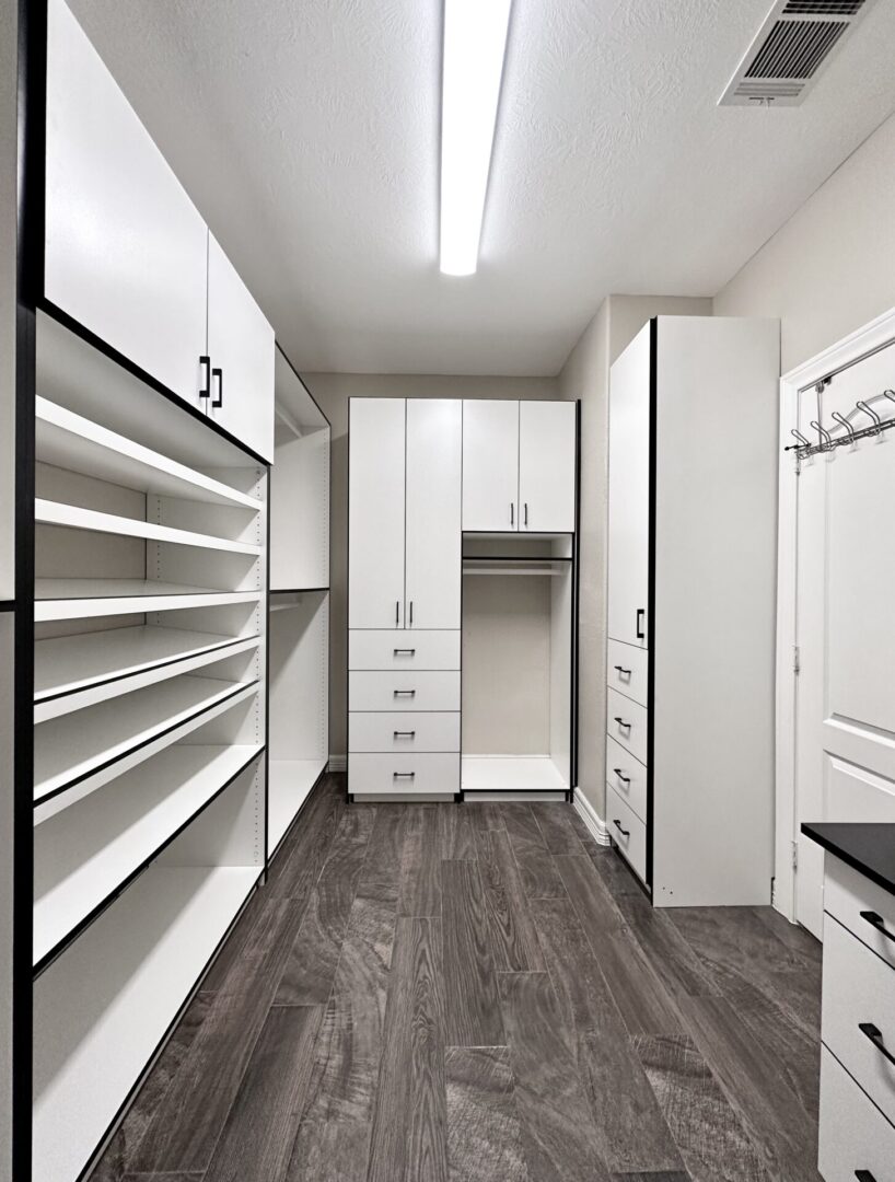 Modern walk-in closet with white cabinetry and built-in shelving, featuring a wood-style flooring.