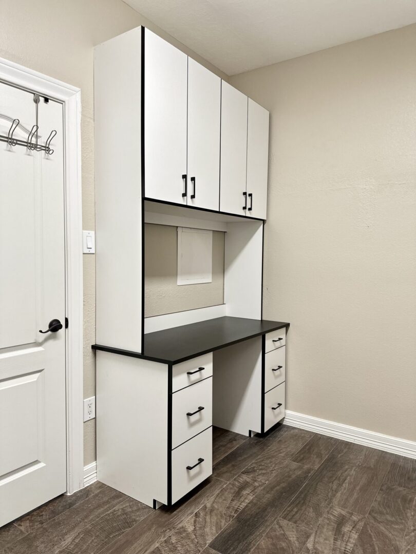 A modern white and black built-in desk with overhead cabinets and drawers in a room with wood flooring.