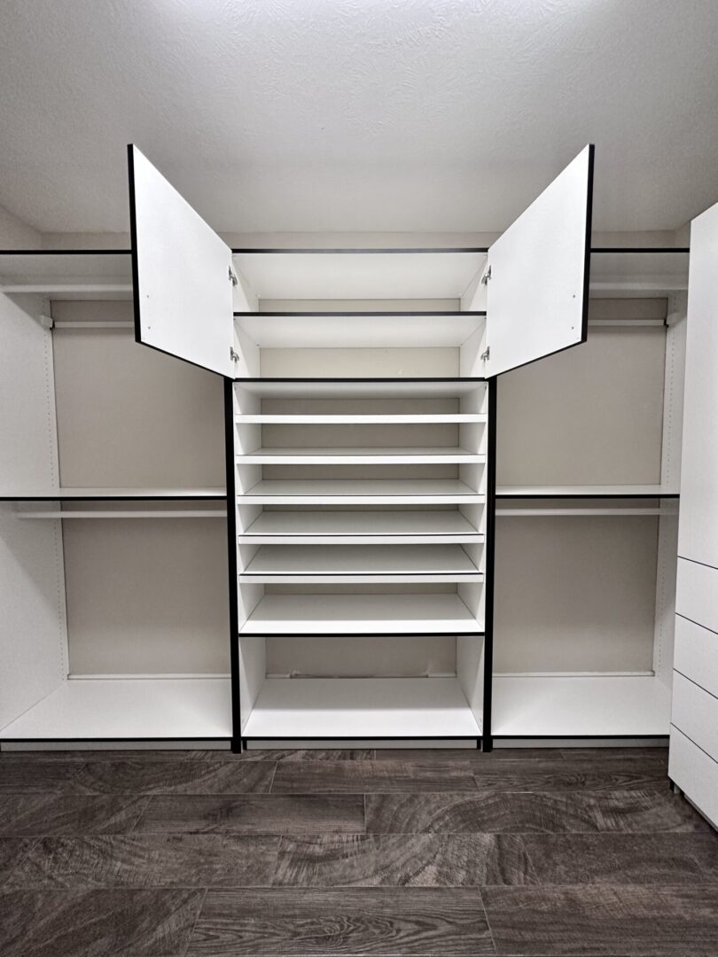 An empty, modern walk-in closet with open white cabinet doors, multiple shelves, and a shoe rack.