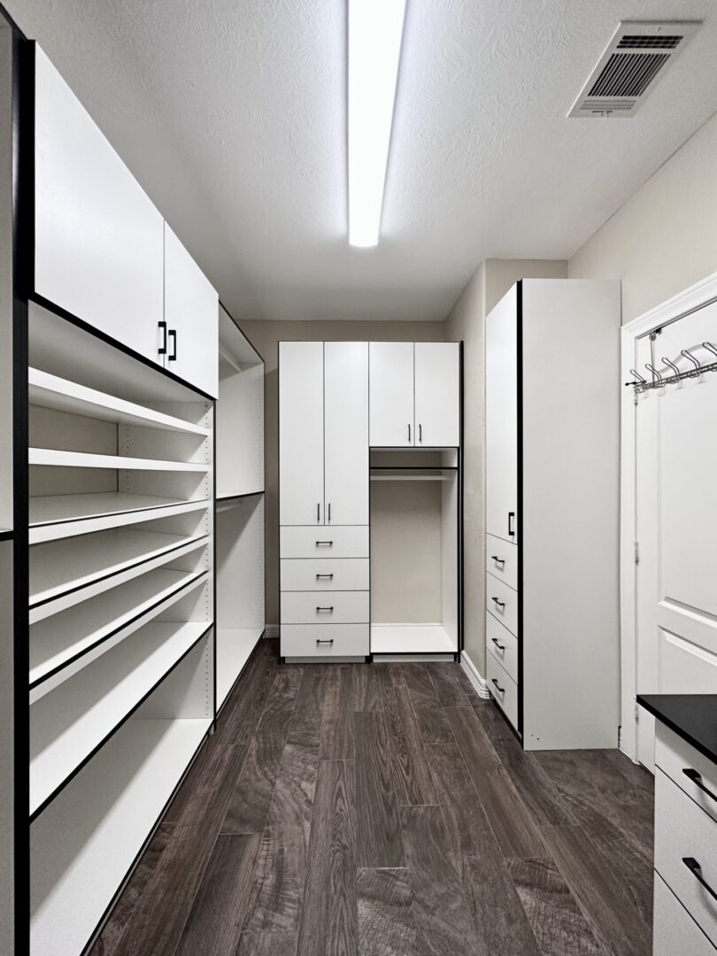 Modern walk-in closet with white cabinetry and built-in shelving, featuring a central dressing area and dark wood flooring.