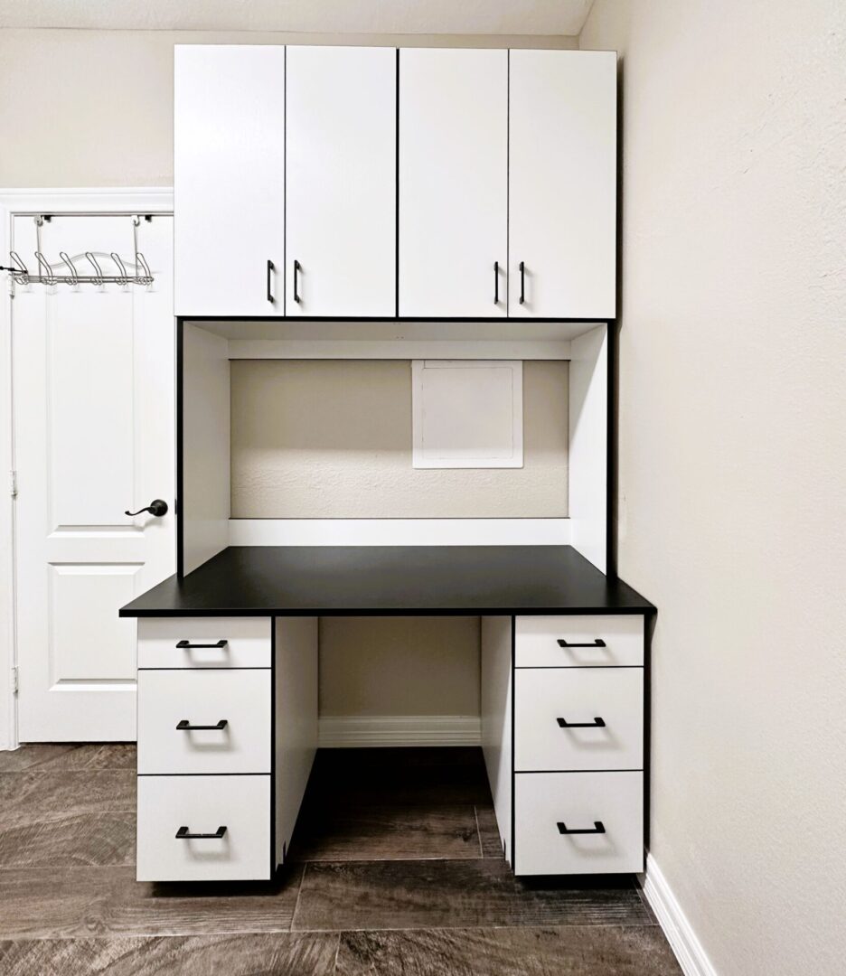 A clean, empty home office nook with white cabinetry and a black desktop.