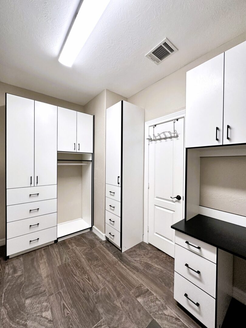 A modern, empty laundry room with white cabinetry and dark wood flooring.