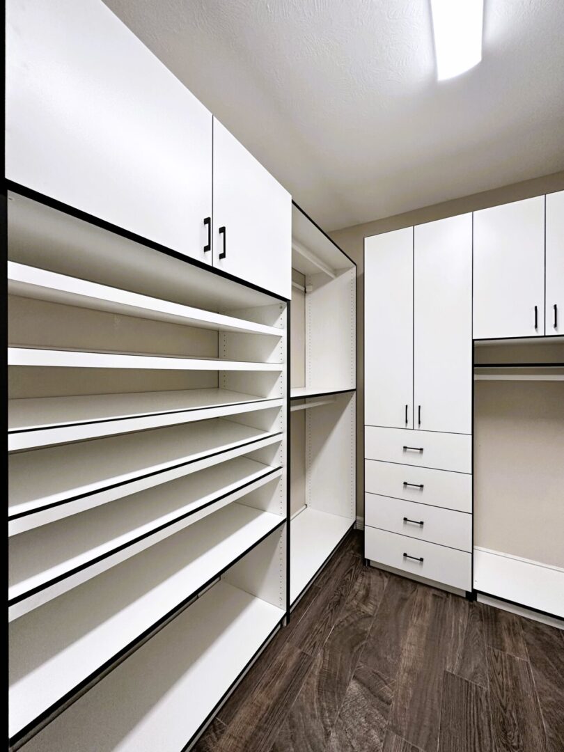 Modern empty walk-in closet with white shelving units and drawers, and dark wood flooring.