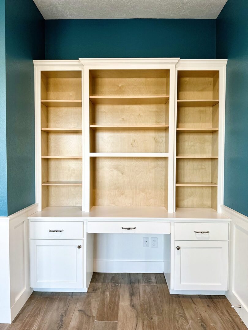 Empty wooden bookshelves integrated with white cabinets against a blue wall in an interior setting, showcasing exceptional custom furnishing.