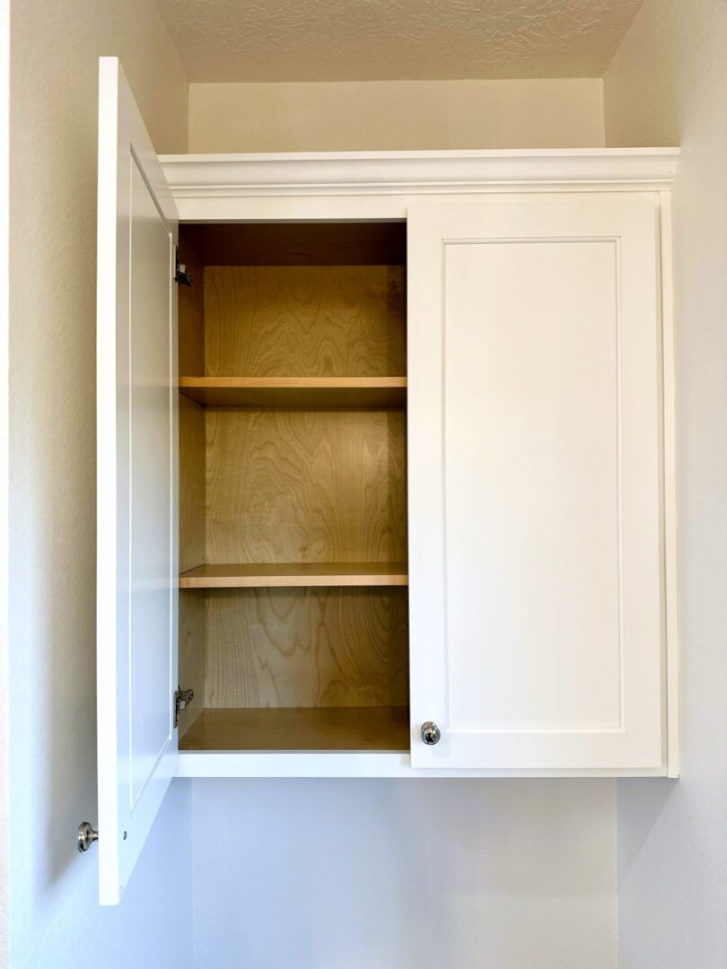 An open, empty white cabinet with two shelves, an exceptional custom furnishing, mounted on a wall.