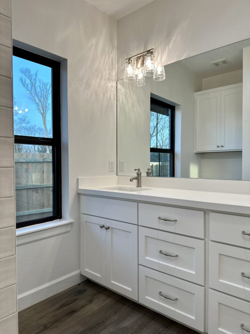 Modern bathroom interior with white vanity, sink, mirror, and a window with a view of bare trees. The exceptional custom furnishing enhances the space's elegance.