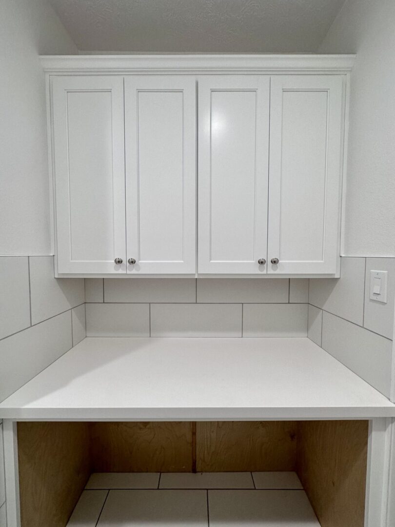 A clean, empty white kitchen countertop with closed white cabinets above, showcasing exceptional custom furnishing.