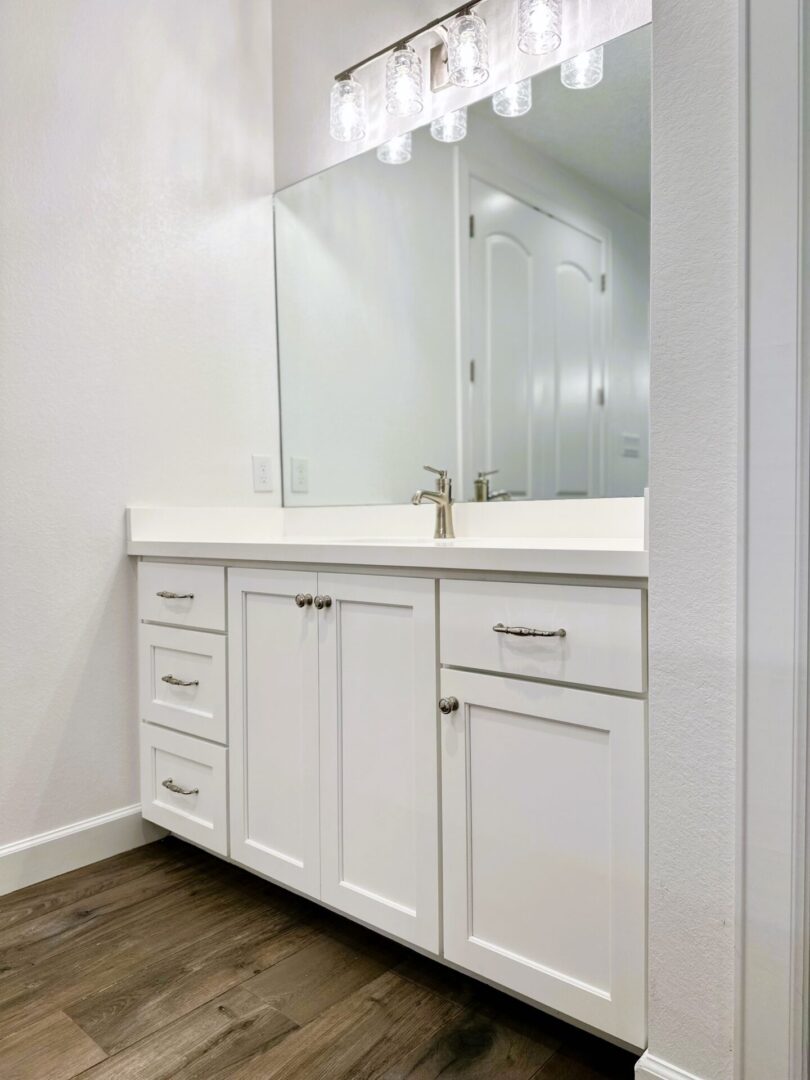 A modern bathroom vanity with white cabinets, a large mirror, and an exceptional custom furnishing light fixture above.