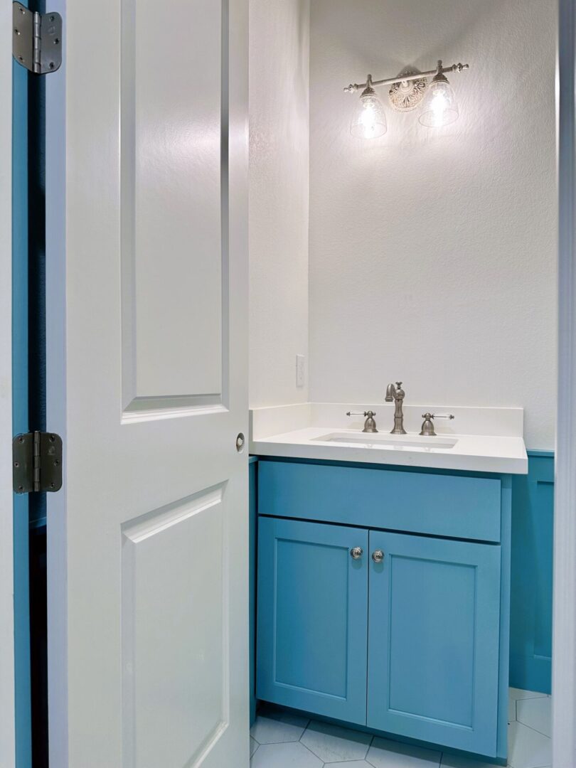 A powder blue bathroom vanity with a white countertop in a small, well-lit room with an open door, boasting exceptional custom furnishing.