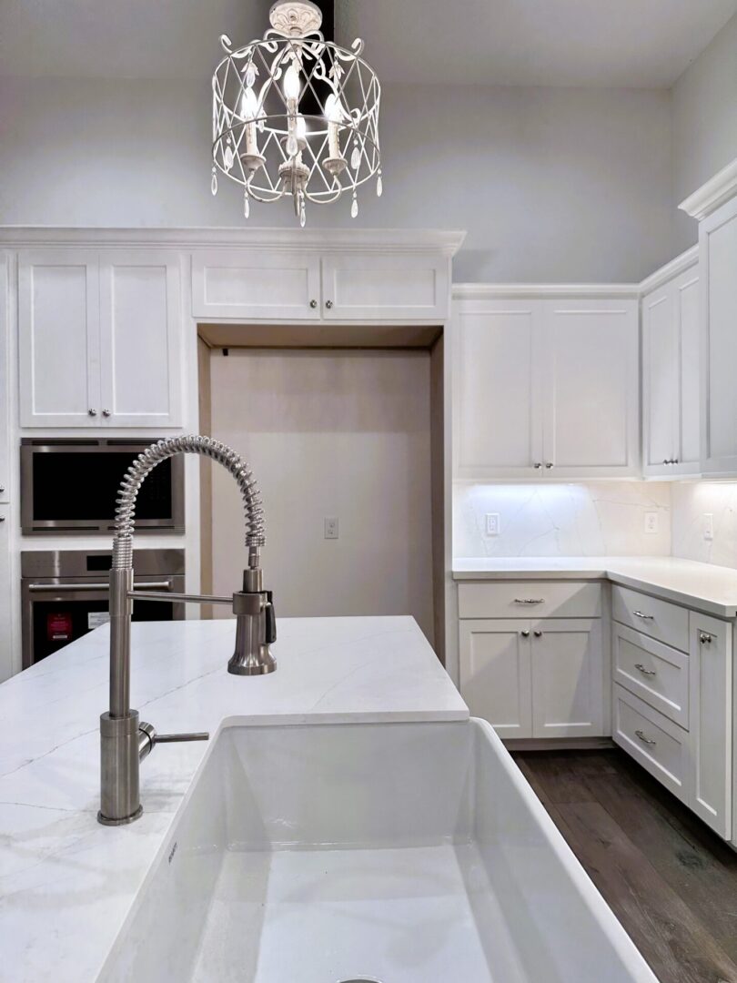 Modern kitchen with white cabinetry, stainless steel faucet, and elegant chandelier, featuring exceptional custom furnishing.