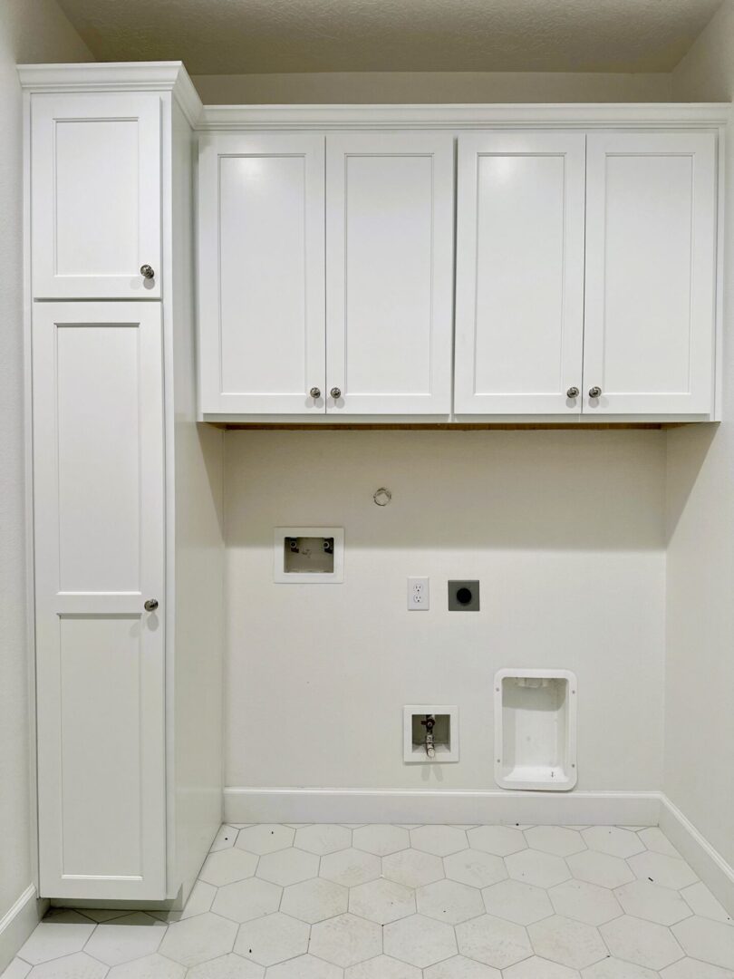 A laundry room with Exceptional Custom Furnishing, featuring white cabinets and an empty space for a washer and dryer.