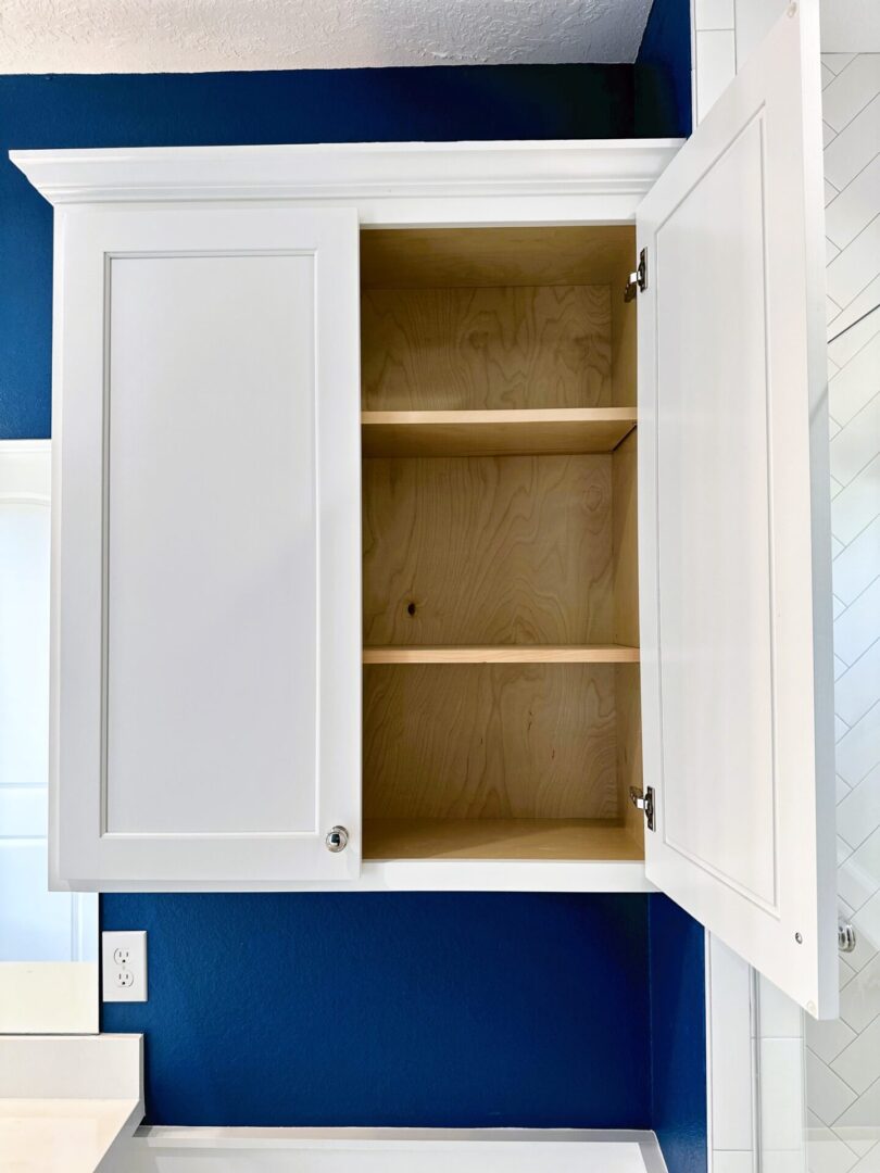 Open white cabinet with empty shelves against a blue wall, featuring exceptional custom furnishing.