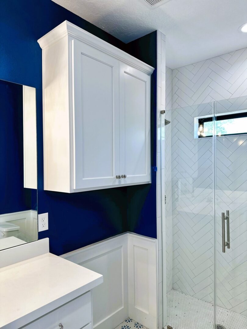 Modern bathroom with exceptional custom furnishing, white cabinetry, and herringbone tiled shower.