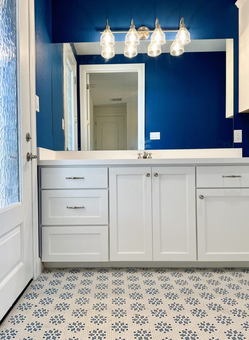 A modern bathroom featuring an exceptional custom furnishing: a white vanity with a matching mirror, set against a vibrant blue wall, and a decorative blue and white tiled floor.