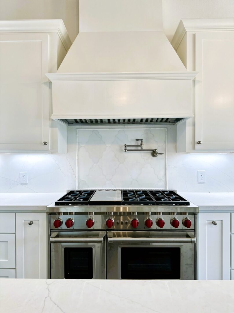 A modern kitchen featuring exceptional custom furnishing, including a stainless steel gas stove with red knobs and a white marble backsplash.