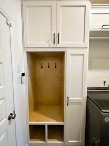 A tall, white, empty cabinet with one door open next to a washing machine in a laundry room.