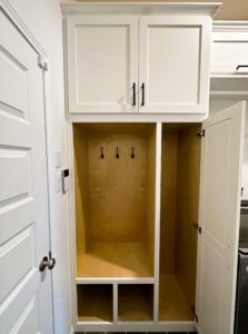 An open, empty white storage cabinet with hooks on the back wall and a closed upper cabinet above.