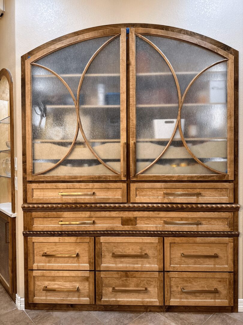 Wooden cabinet with glass doors and multiple drawers in a domestic setting.