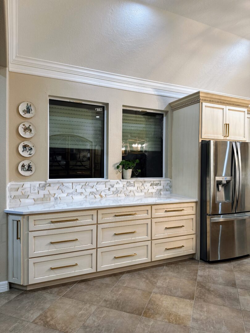 A modern kitchen featuring stainless steel refrigerator next to a white cabinet with drawers and decorative plates on the wall.