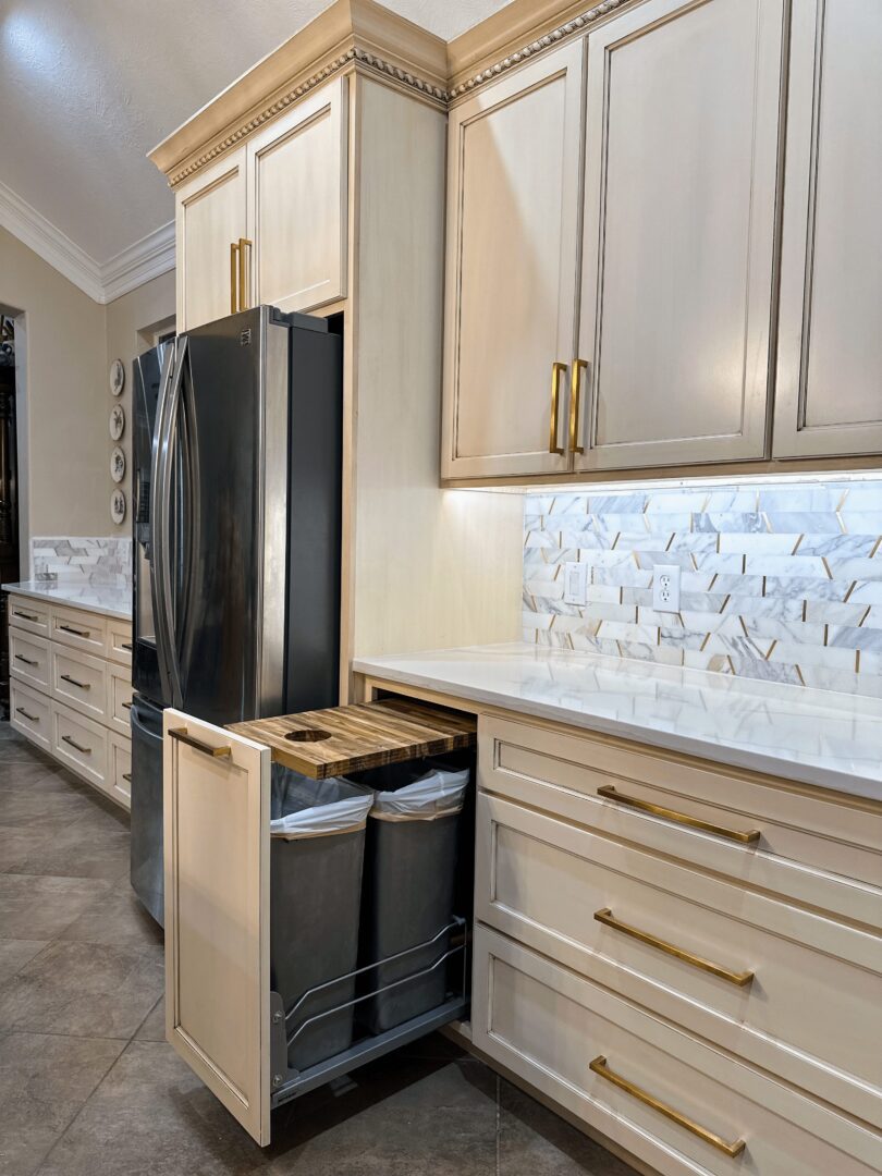 A modern kitchen interior featuring stainless steel appliances, white cabinetry with gold handles, and a herringbone-patterned backsplash.