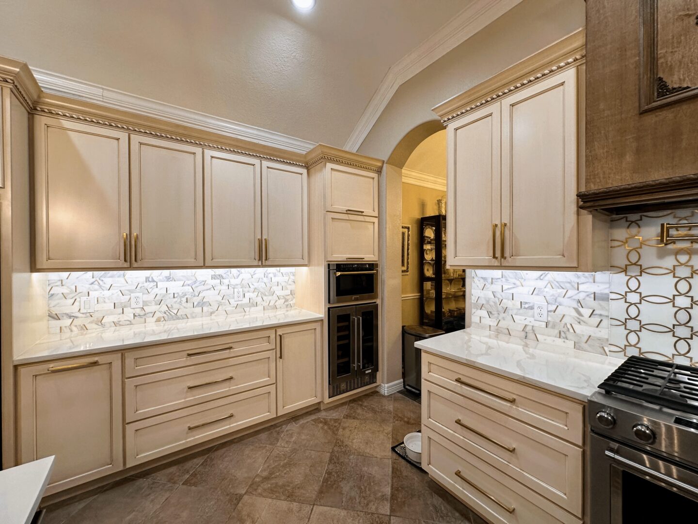 A modern kitchen with beige cabinetry, stainless steel appliances, and a geometric backsplash.