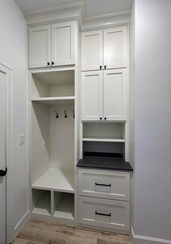 An exceptional custom white built-in hallway storage unit with cabinets, hooks, and drawers.