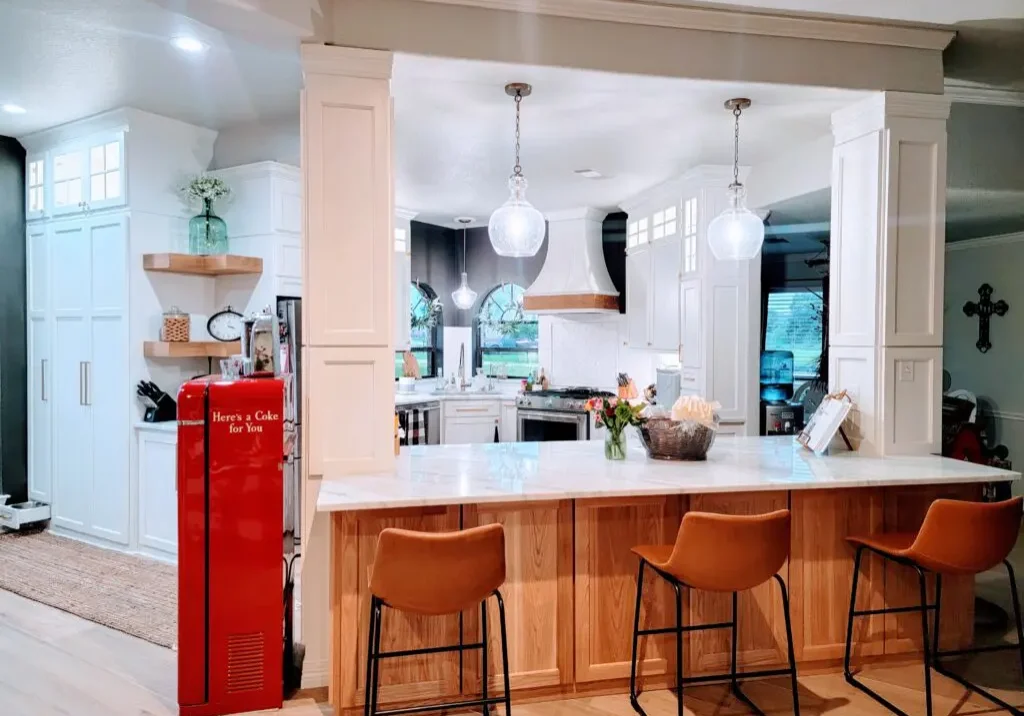 A bright and modern kitchen with white cabinetry, a wooden island with seating, pendant lights, and a red retro-style refrigerator featuring exceptional custom furnishing.